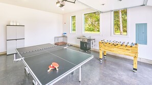 Ein Tischtennis-Tisch, ein Fußballtisch und eine Küchenzeile in einem Raum mit Fenstern und einer Tür.