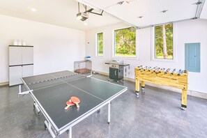 Ein Tischtennis-Tisch, ein Fußballtisch und eine Küchenzeile in einem Raum mit Fenstern und einer Tür.
