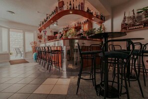 Eine Barbereich mit einer gebogenen Holztrennwand, an der Flaschen stehen, einer Bar und mehreren schwarzen Barhocker.