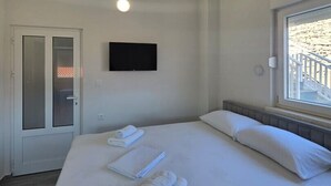 Una camera d'albergo con un letto, una TV a muro, una finestra con vista e una porta.