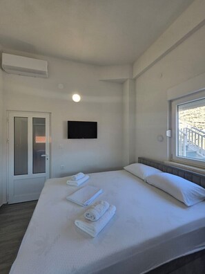 Ein Hotelzimmer mit einem Bett, einem an der Wand befestigten Fernseher, einem Fenster mit Blick und einer Tür.