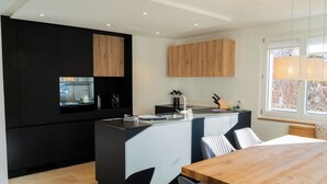 Eine moderne Küche mit schwarzen und hölzernen Schränken, einer zentralen Kochinsel und einem Essbereich mit einem Holztisch und Stühlen.