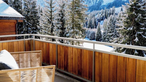 Ein Balkon mit Holzwertung, Korbmöbeln und Blick auf schneebedeckte Bäume und Berge.