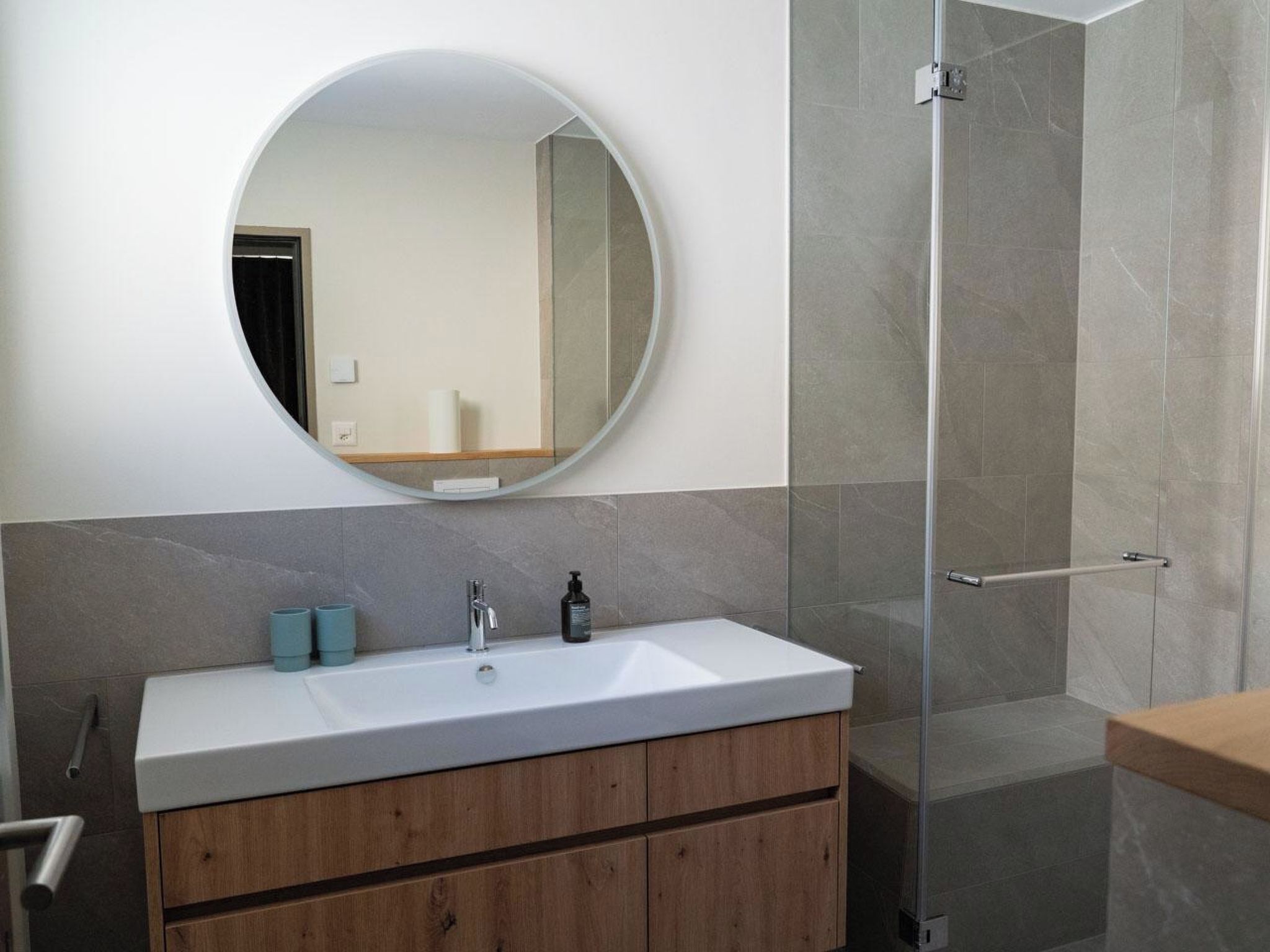 Een moderne badkamer met een ronde spiegel, een witte wastafel en een douchecabine.