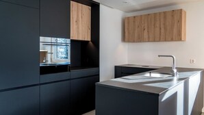 Eine moderne Küche mit schwarzen Schränken, einem Holzschrank oben, einer Spüle aus Edelstahl und einem Fenster.