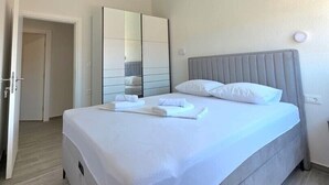 Una cama bien hecha con sábanas blancas, cabecera gris y un espejo grande encima.
