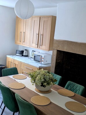 A modern kitchen with wooden cabinets, a microwave, a toaster, and a dining table with green chairs. - Luxury Retreat Contractors| Business| Families (Tow Law)