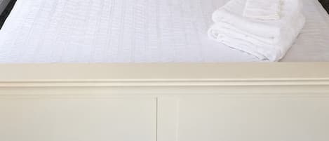 A neatly made bed with a quilted white bedspread, a decorative pillow, and folded towels on the side.