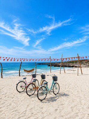 A beach with bicycles parked on the sand, a hammock, and a swing set.