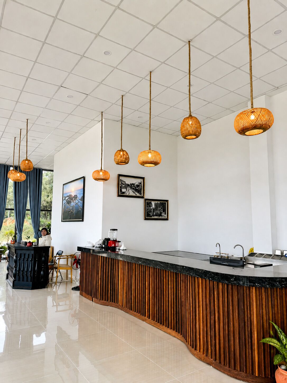A modern hotel lobby with a curved reception desk, hanging wicker pendant lights, and framed artwork on the walls.