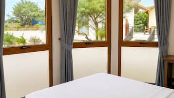 A bedroom with a large bed, two windows with curtains, and a view of the outdoors.