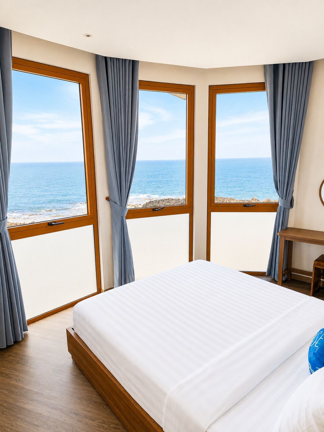 Une chambre d’hôtel avec un lit, un bureau et une vue sur la mer, grâce à de grandes fenêtres.