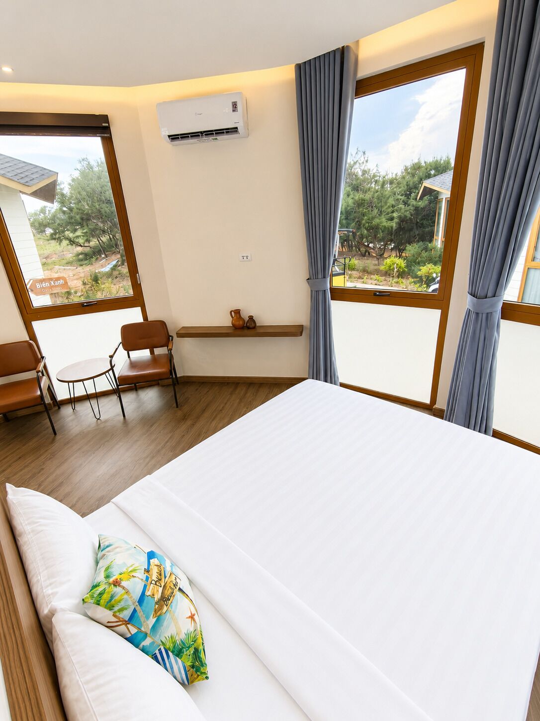 Een hotelkamer met een groot bed, een kleine tafel met stoelen, een airconditioning en uitzicht op het omliggende landschap.