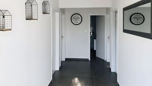 Um corredor com chão de azulejos, paredes brancas e dois quadros nas paredes.