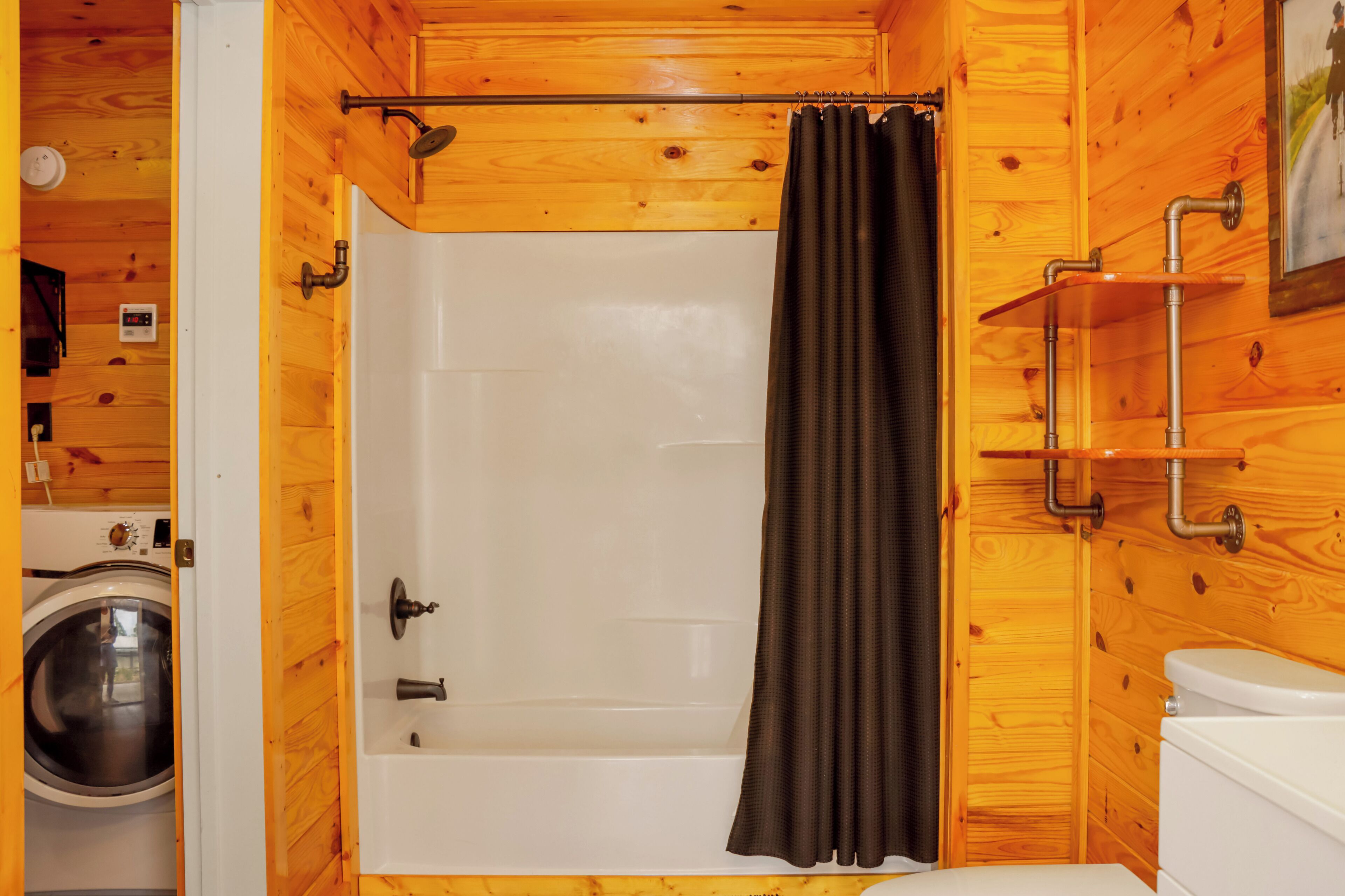 Une salle de bain rustique, située dans une cabane en bois, équipée d’une douche, de toilettes et d’un lave-linge.