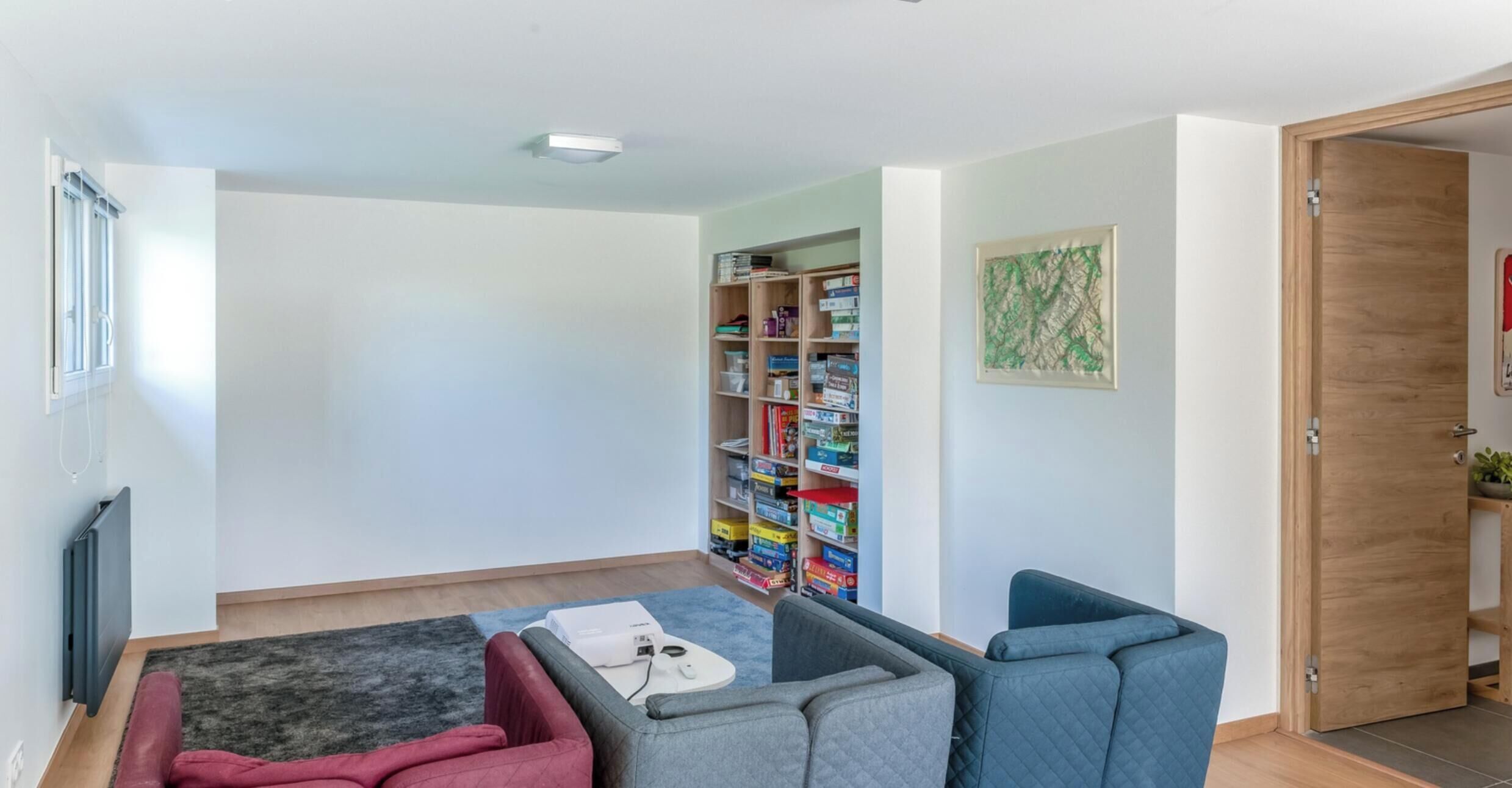 Un salon moderne avec un canapé d’angle, une petite table et une bibliothèque remplie de jeux de société.
