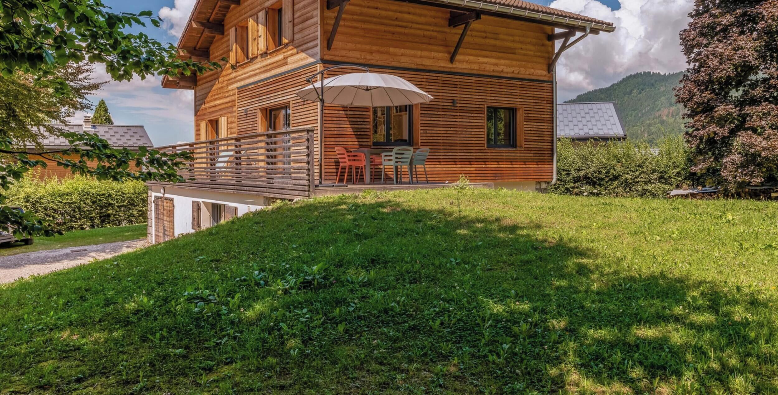A wooden chalet with a balcony, outdoor seating, and a view of a mountainous landscape.