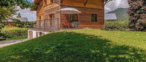 A wooden chalet with a balcony, outdoor seating, and a view of a mountainous landscape.