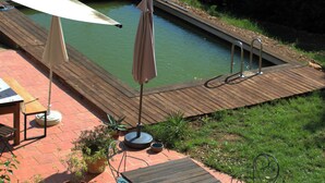 Una terraza de madera con piscina, mobiliario exterior y plantas en macetas.