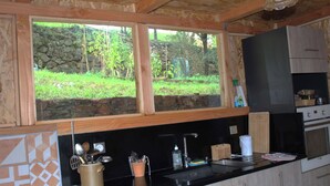 Cocina con pared de piedra, vigas de madera, encimera negra y vistas a zonas verdes.