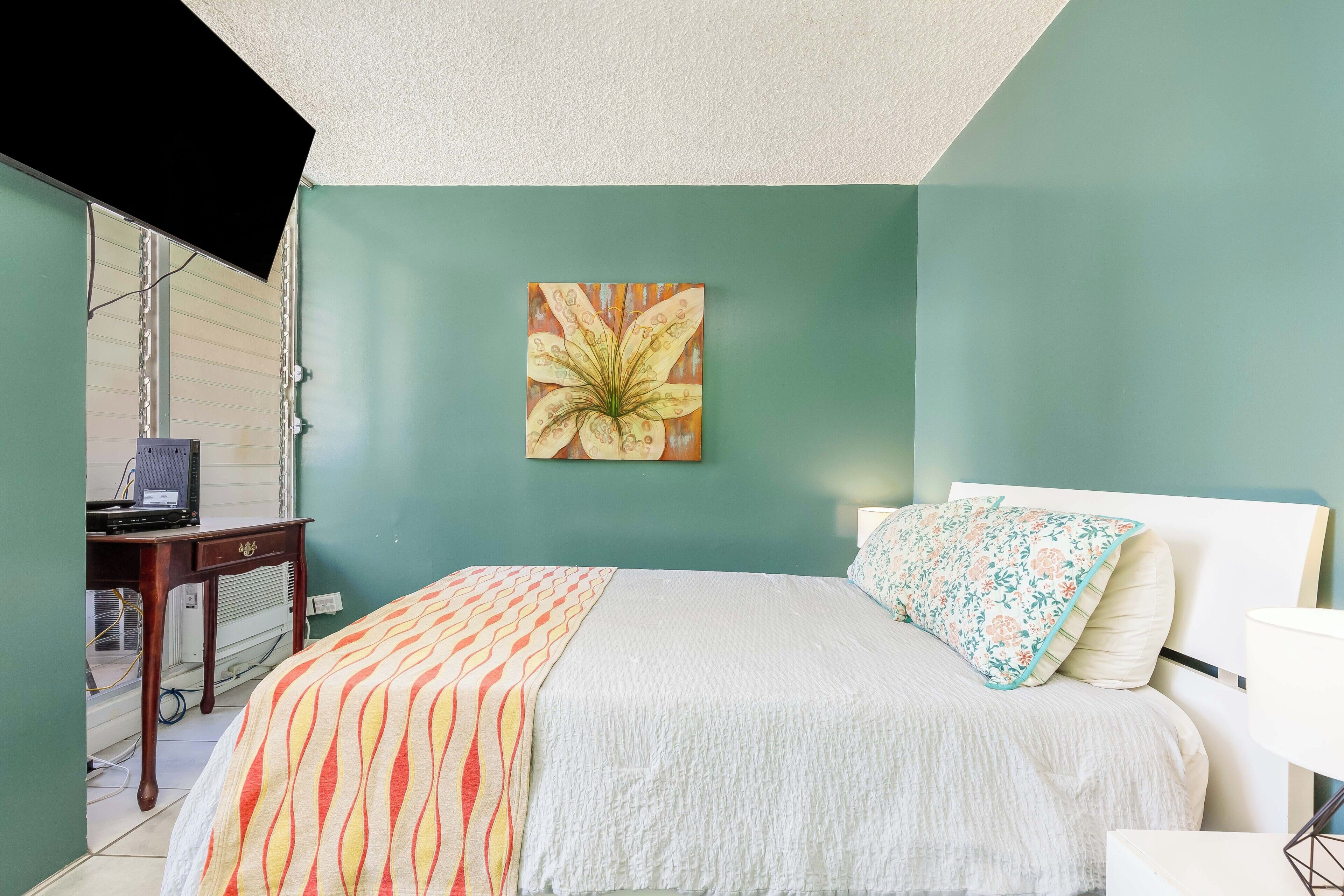 A bedroom with a bed, a desk, and a wall-mounted TV.