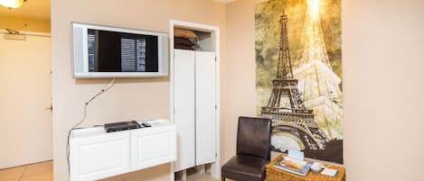Una habitación con un armario blanco, un televisor montado, una cesta de mimbre y un mural en la pared de la Torre Eiffel.