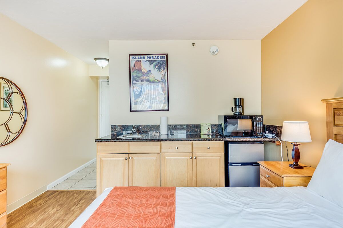 Une chambre d’hôtel avec un lit, une petite kitchenette, une machine à café, une lampe et une affiche au mur.