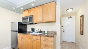 A kitchen with wooden cabinets, a stainless steel refrigerator, a microwave, and a granite countertop. - Chic Studio w/Kitchenette, Lanai, AC, WiFi–Waikīkī Grand #501 (Honolulu)