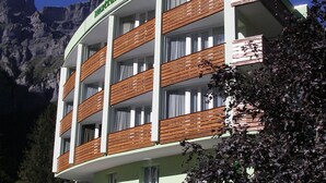 Un hotel de varios pisos con balcones, un paisaje montañoso de fondo y un letrero que indica que es un hotel.