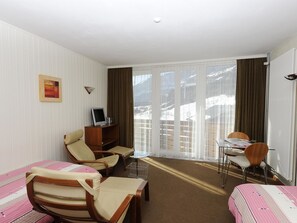 Habitación de hotel con dos camas, un escritorio, una silla, televisión y vistas a un paisaje nevado a través de las ventanas.