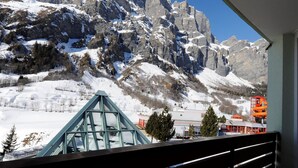 Vista de la montaña desde un balcón, con picos nevados, una estructura de cristal y un edificio rojo al frente.