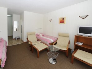 Une pièce comprenant un lit, deux chaises, une petite table, un téléviseur et un tableau accroché au mur.