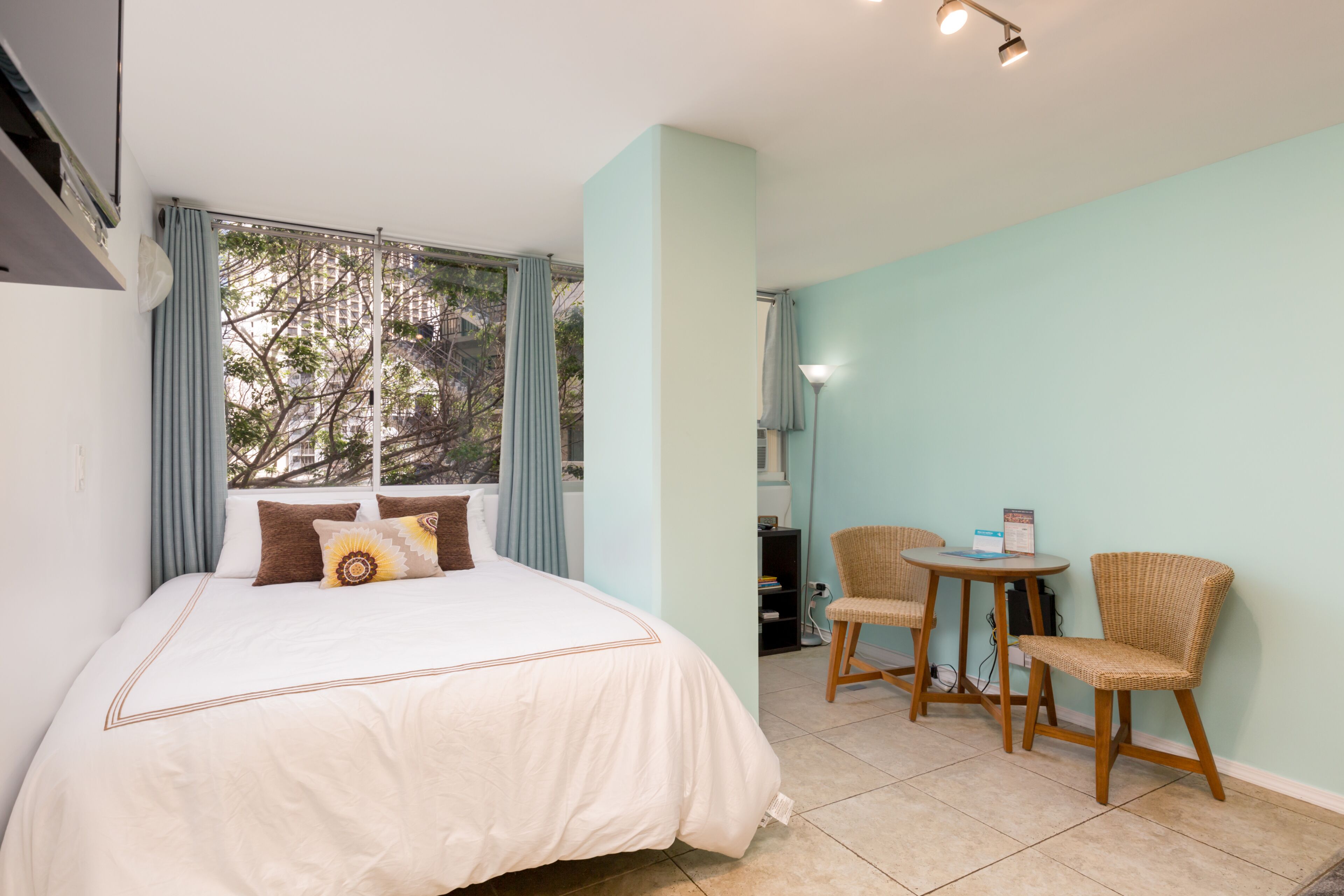 Ein Schlafzimmer mit einem Bett, zwei Stühlen, einem Tisch und einem Fenster mit Vorhängen.