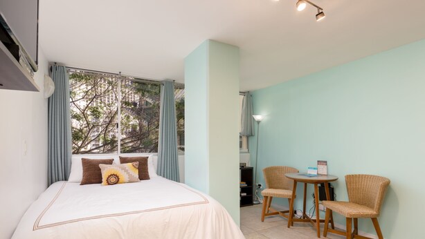 A bedroom with a bed, two chairs, a table, and a window with curtains. - High-Style Studio w/Kitchenette, WiFi, Flat Screen+AC–Waikiki Grand 503 (Honolulu)