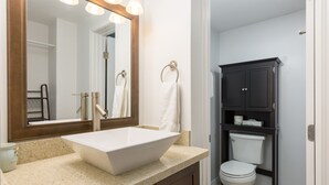 A bathroom with a large mirror, a white sink, a toilet, and a dark cabinet. - High-Style Studio w/Kitchenette, WiFi, Flat Screen+AC–Waikiki Grand 503 (Honolulu)