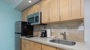 A kitchen with wooden cabinets, a stainless steel sink, a microwave, and a refrigerator. - High-Style Studio w/Kitchenette, WiFi, Flat Screen+AC–Waikiki Grand 503 (Honolulu)