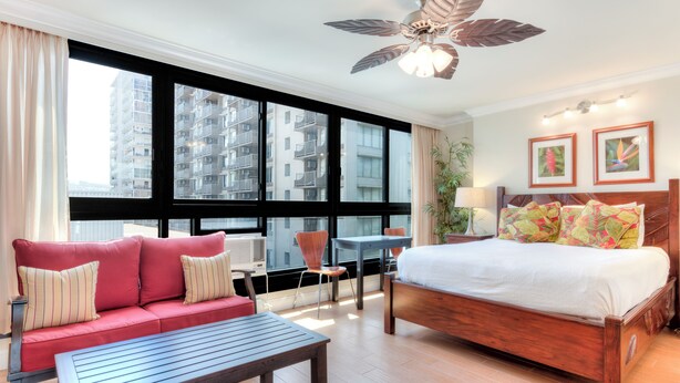 Habitación de hotel con cama, sofá, mesa, escritorio y una ventana grande con vistas a edificios altos.
