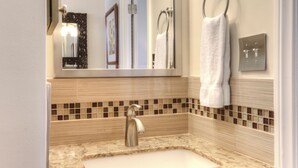 Baño con lavamanos, espejo, argolla para toallas y una lámpara.