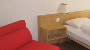 Ein Zimmer mit einem roten Sofa, einem Nachttisch aus Holz mit Lampe und einem Bett mit weißer Bettwäsche.