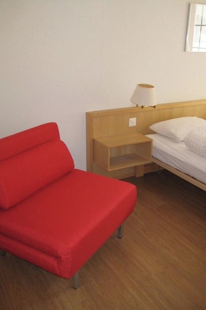 A room with a red sofa, a wooden nightstand with a lamp, and a bed with white bedding. - Les Naturelles B 306 # 6-bed apartment, Dusche und Bad, WC by Interhome (Leukerbad)