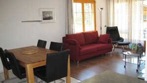 Ein Wohnzimmer mit einem Holzesstisch, schwarzen Stühlen, einem roten Sofa, einem schwarzen Sessel und einem Glastisch.