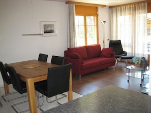 A living room with a wooden dining table, black chairs, a red sofa, a black armchair, and a glass coffee table. - Les Naturelles B 306 # 6-bed apartment, Dusche und Bad, WC by Interhome (Leukerbad)