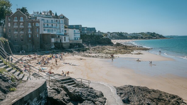 Un hotel costero de varios pisos, con una playa al fondo y un litoral rocoso.