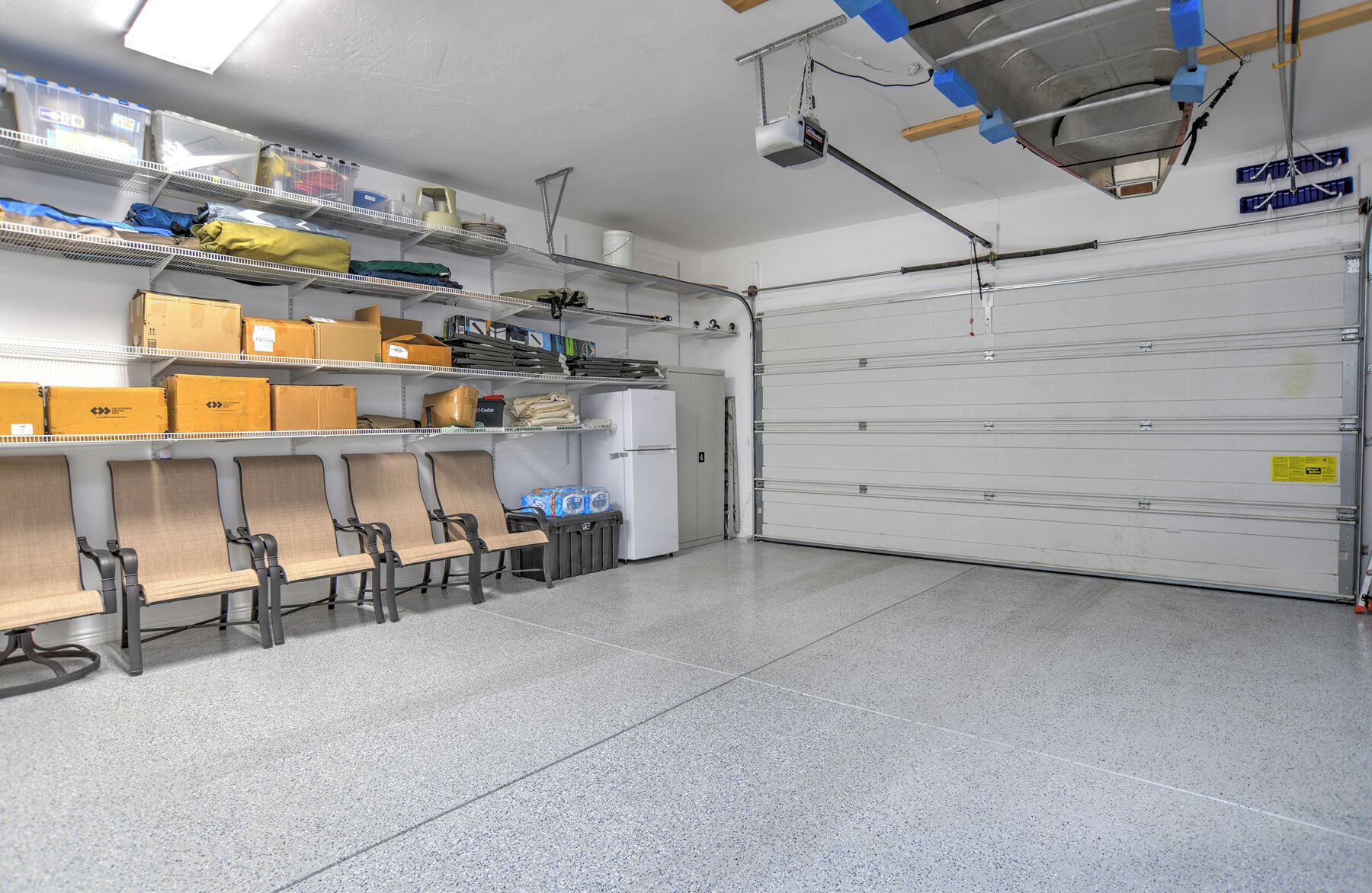 A clean, well-organized storage area with metal shelving, chairs, and a large garage door.