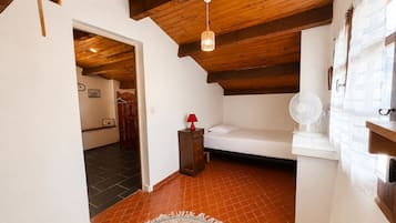 A bedroom with a wooden ceiling, a bed, a fan, a red lamp, and a small table.