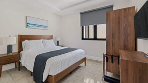 A bedroom with a bed, bedside tables, a TV stand, and a window with a view. - Cozy 2BR in Miramar | Kitchen, Laundry & TVs (San Juan)