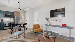 A modern kitchen with a built-in oven and microwave, a dining area with a table and chairs, and a living space with a sofa and a TV mounted on the wall. - Cozy 2BR in Miramar | Kitchen, Laundry & TVs (San Juan)