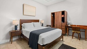 Quarto com cama, mesas de cabeceira, escrivaninha e guarda-roupa.