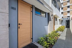 A modern building with a large wooden door, a number '102' sign, and a narrow walkway with plants. - Stylish Studio in Miramar | Work Desk + Smart TV (San Juan)