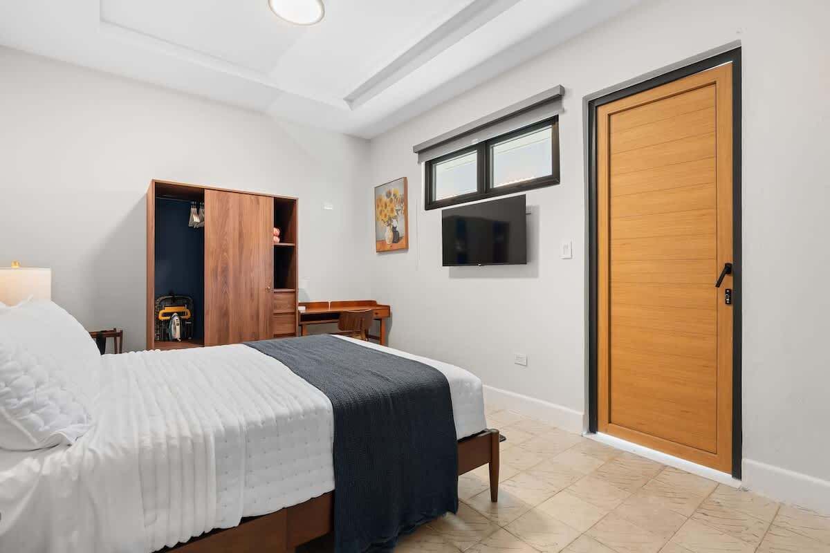 A bedroom with a bed, a wardrobe, a desk, a television, and a door.